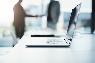 Buy stock photo Shot of a laptop on a boardroom desk with two businessmen blurred in the background