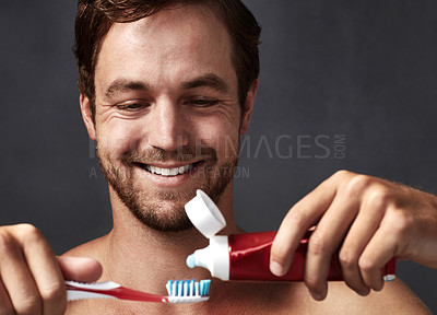 Buy stock photo Cropped shot of a handsome young man putting toothpaste on his toothbrush