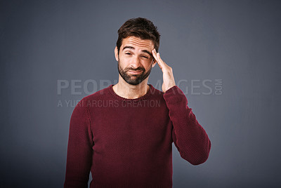Buy stock photo Studio shot of a handsome young man suffering from a headache against a gray background