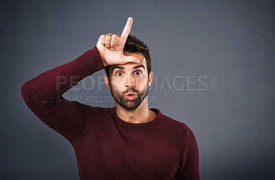 Buy stock photo Studio shot of a young man showing a ‘loser’ sign on his forehead against a gray background