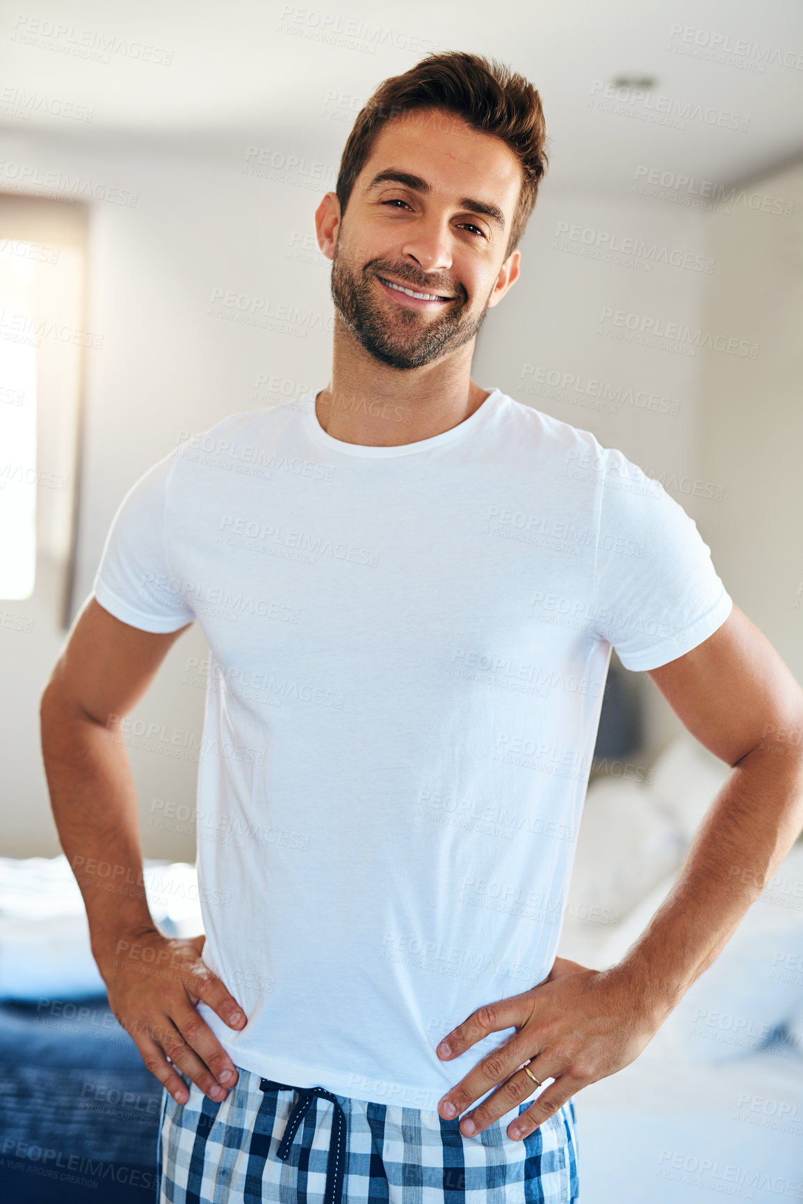 Buy stock photo Cropped portrait of a handsome young man standing with his hands on his hips in his bedroom at home