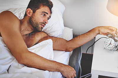 Buy stock photo Cropped shot of a handsome young man turning off the alarm after waking up in his bedroom at home