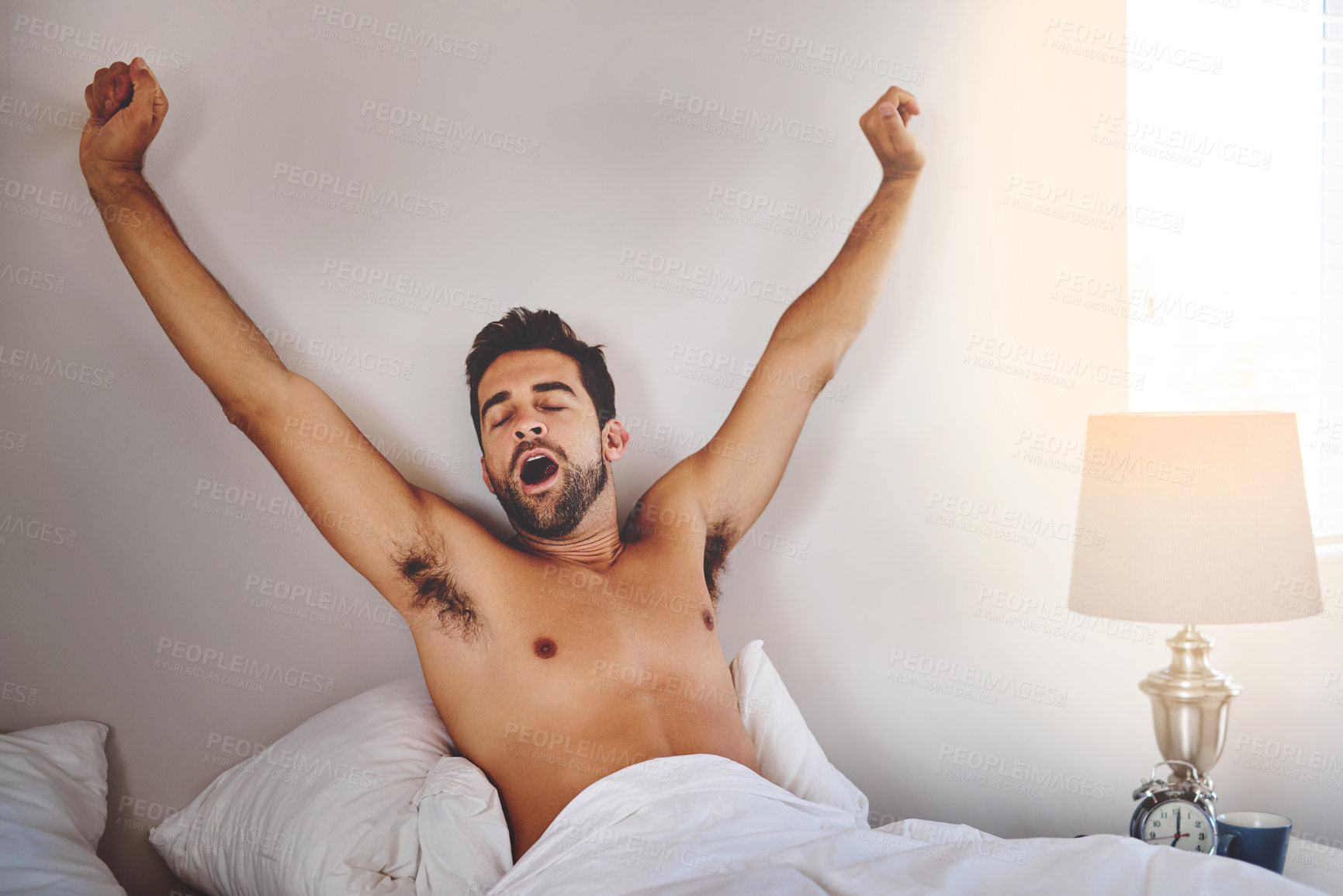 Buy stock photo Cropped shot of a handsome young man stretching while waking up in his bedroom at home