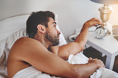 Buy stock photo Cropped shot of a handsome young man turning off the alarm after waking up in his bedroom at home