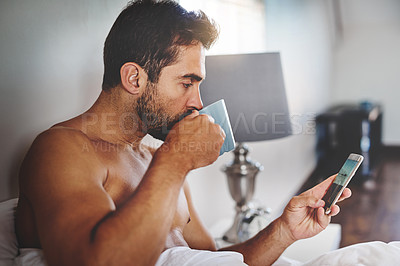 Buy stock photo Cropped shot of a handsome young man checking his messages while drinking coffee in his bed at home