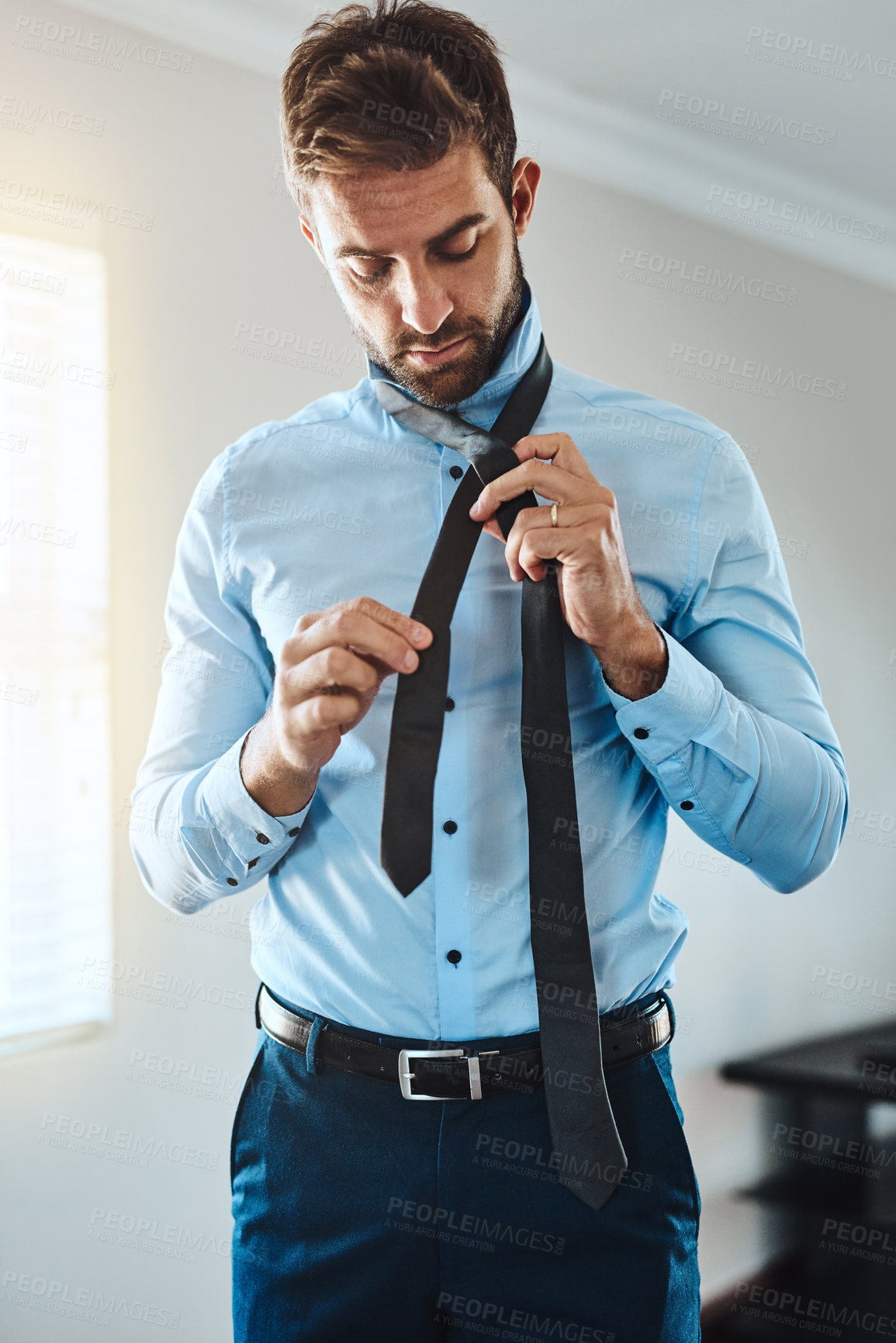 Buy stock photo Cropped shot of a handsome young man putting on a tie in his bedroom at home