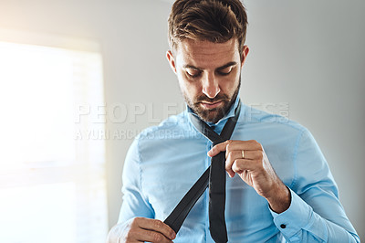 Buy stock photo Cropped shot of a handsome young man putting on a tie in his bedroom at home