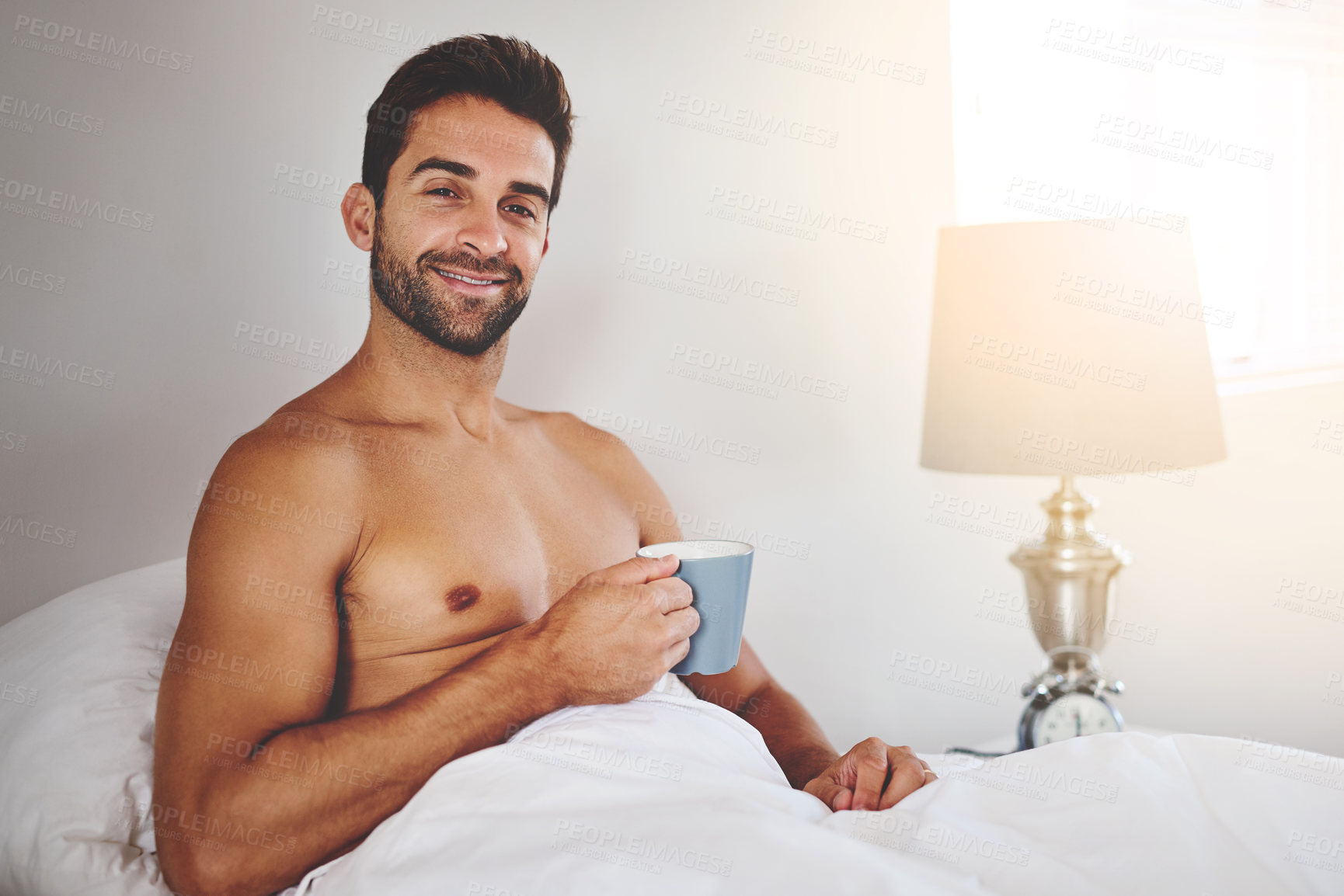 Buy stock photo Portrait, bedroom and man with coffee, morning and smile with happiness, lamp and hospitality. Face, bed and house with guy, person and herbal tea with cappuccino, lodge and relax with accommodation