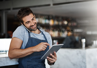 Buy stock photo Shot of a young man using a digital tablet and mobile phone while working at a coffee shop
