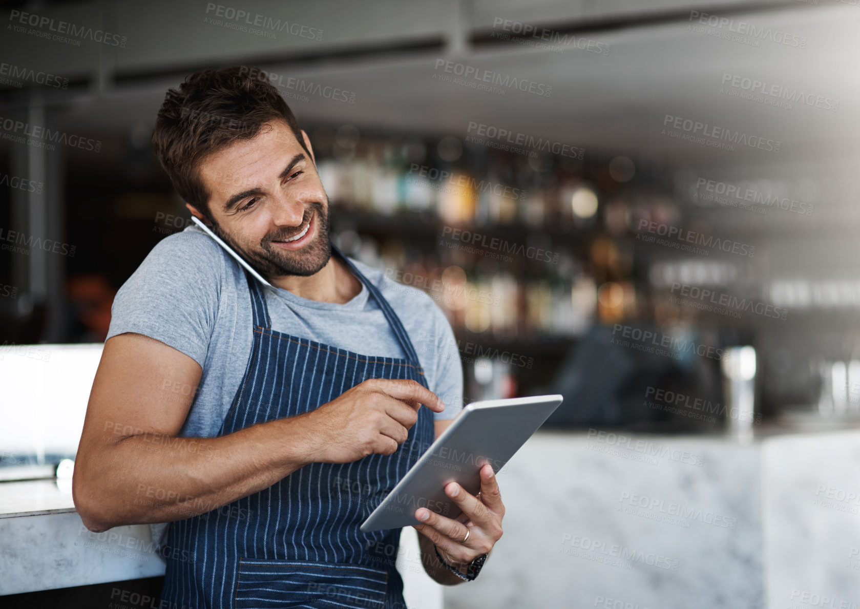 Buy stock photo Shot of a young man using a digital tablet and mobile phone while working at a coffee shop