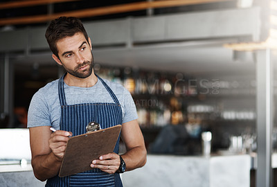 Buy stock photo Shot of a young man using a clipboard while working in a bar