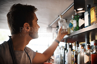 Buy stock photo Shot of a young man looking at the merchandise on the shelves behind a bar counter