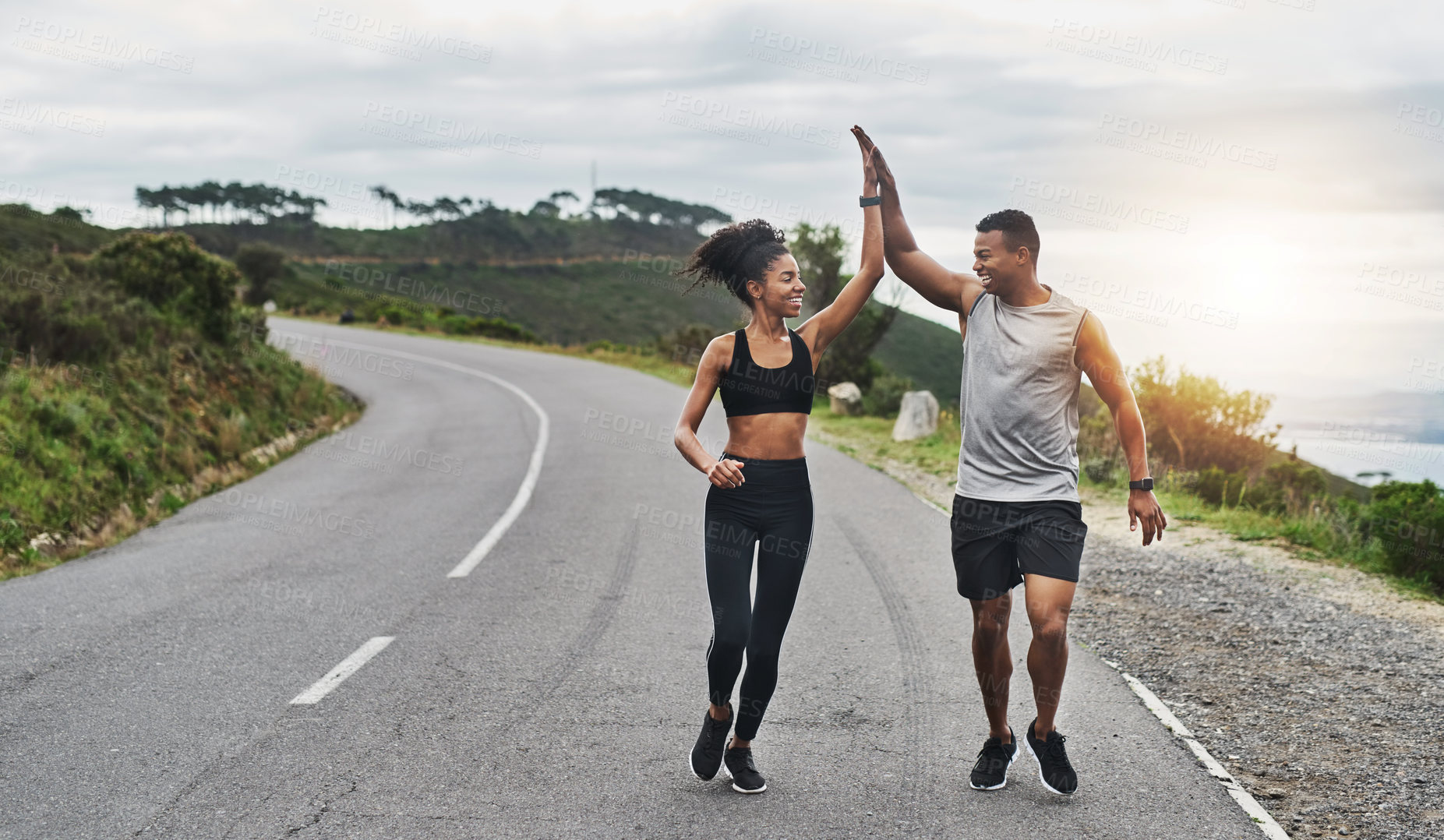 Buy stock photo Shot of a sporty young couple high fiving each other while exercising outdoors