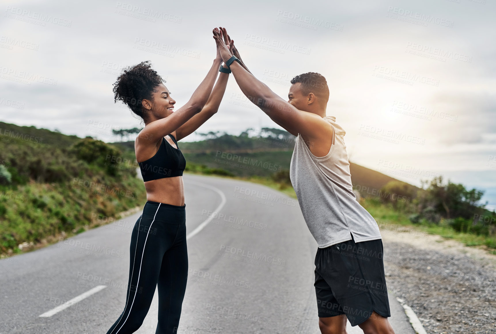 Buy stock photo Shot of a sporty young couple high fiving each other while exercising outdoors