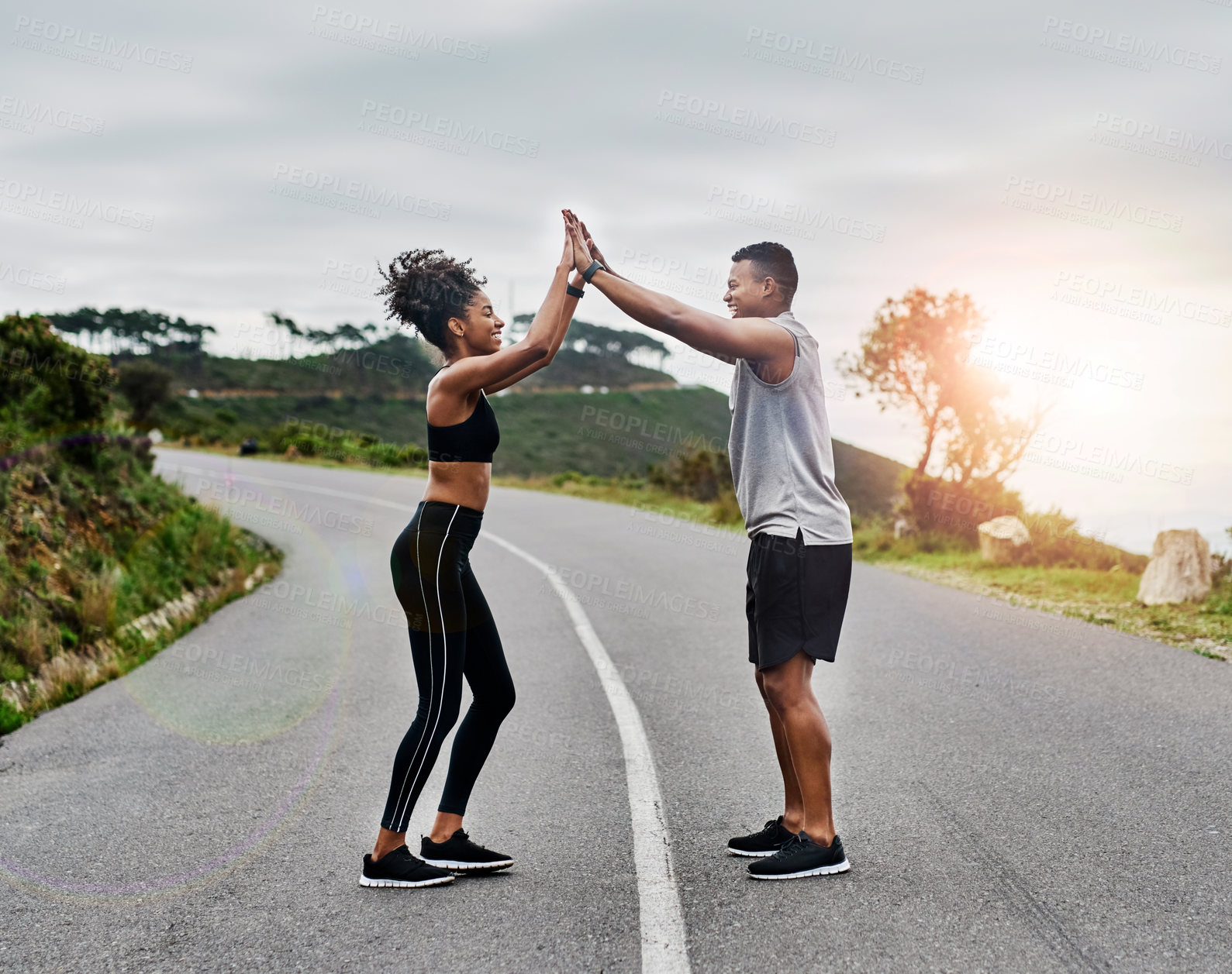 Buy stock photo Shot of a sporty young couple high fiving each other while exercising outdoors