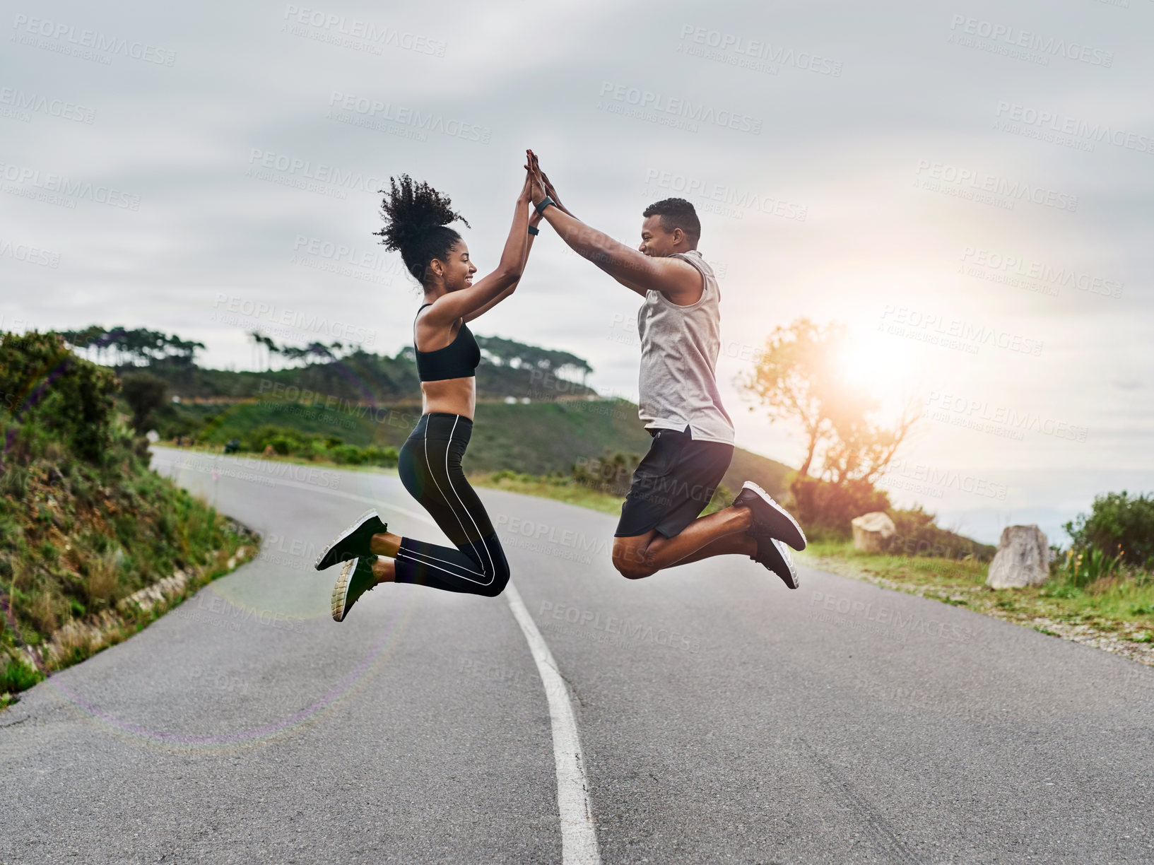 Buy stock photo Shot of a sporty young couple high fiving each other while exercising outdoors