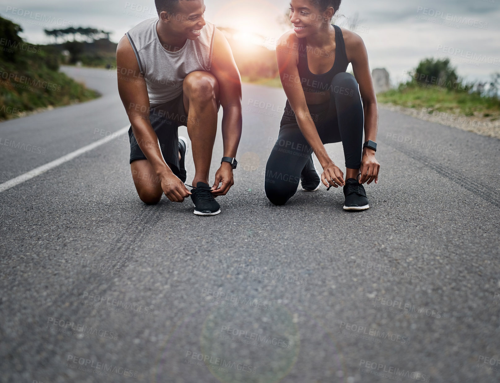 Buy stock photo Shot of a sporty young couple tying their shoelaces while exercising outdoors