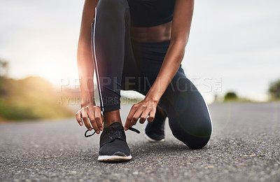 Buy stock photo Closeup shot of a sporty woman tying her shoelaces while exercising outdoors