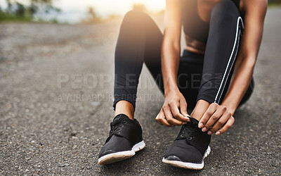 Buy stock photo Closeup shot of a sporty woman tying her shoelaces while exercising outdoors