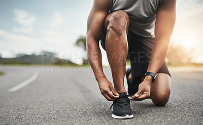 Buy stock photo Closeup shot of a sporty man tying his shoelaces while exercising outdoors