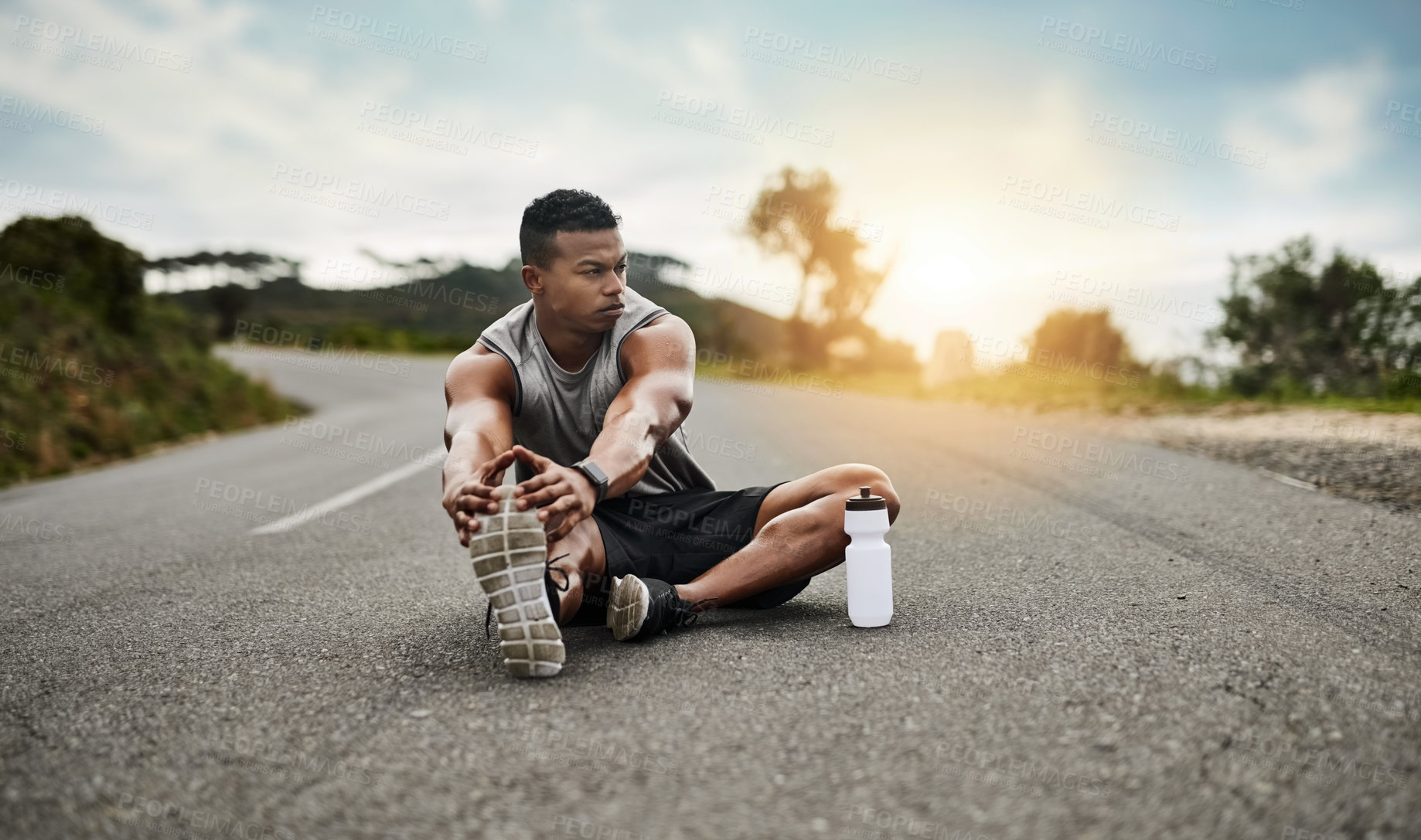 Buy stock photo Shot of a sporty young man stretching his legs while exercising outdoors