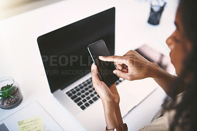 Buy stock photo Shot of a young businesswoman using a mobile phone and laptop at her desk in a modern office