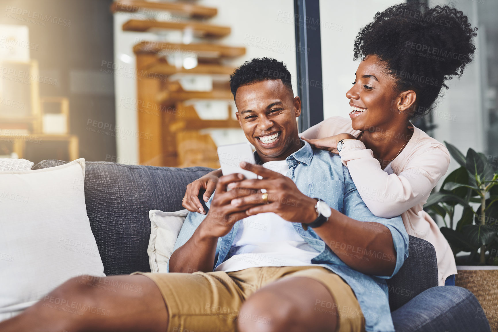 Buy stock photo Shot of a happy young couple using a mobile phone together on the sofa at home