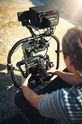 Buy stock photo Over the shoulder shot of an unrecognizable young man making adjustments on a state of the art video camera before shooting a scene on a beach