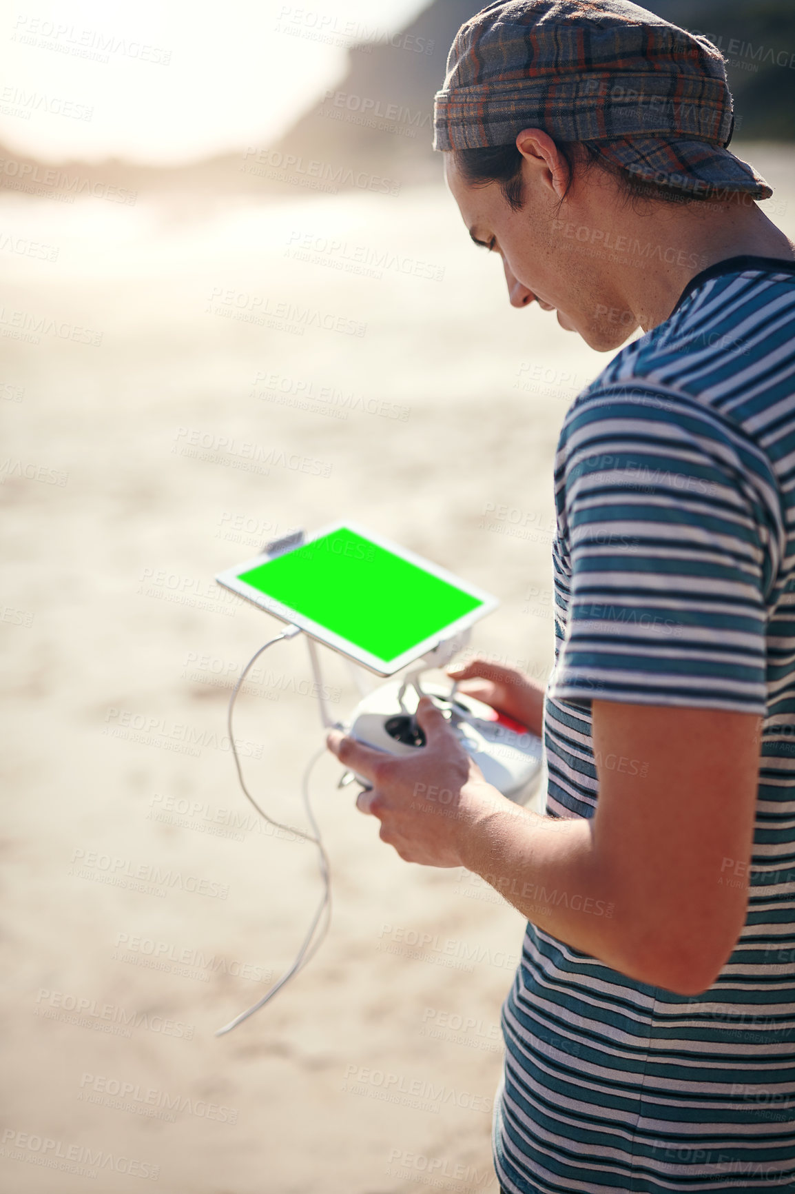 Buy stock photo Shot of a focused young man holding a remote control to fly a drone on a beach outside during the day