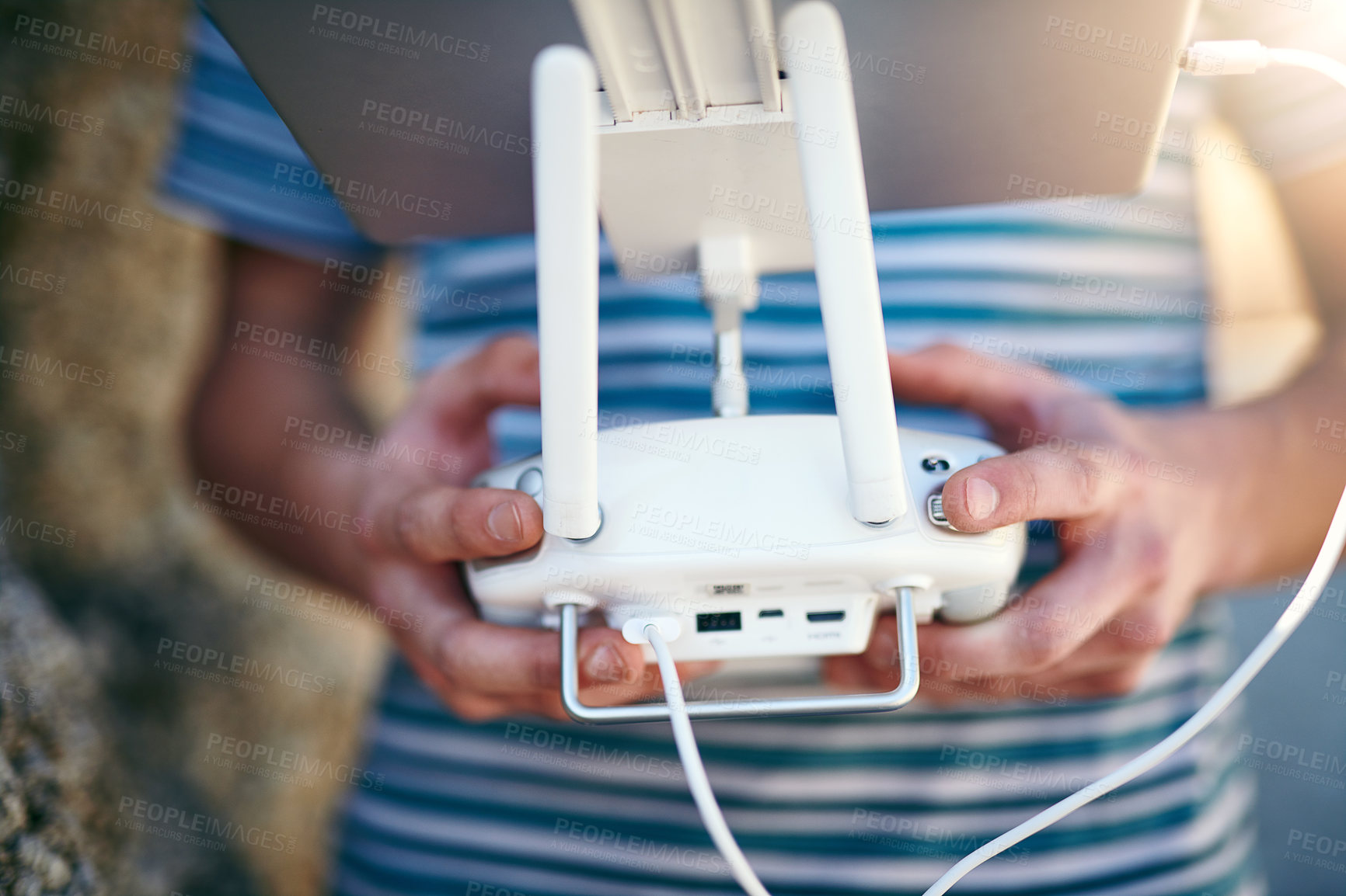 Buy stock photo Closeup of an unrecognizable man holding a remote control and using it to fly a drone outside on a beach during the day