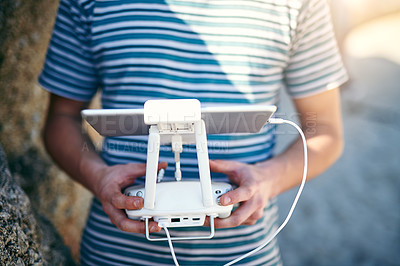 Buy stock photo Closeup of an unrecognizable man holding a remote control and using it to fly a drone outside on a beach during the day