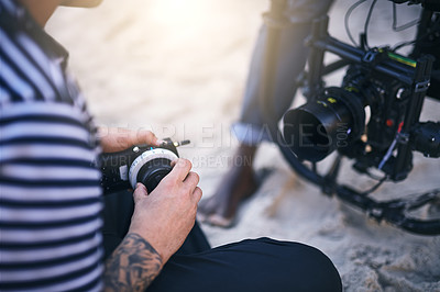 Buy stock photo Closeup of an unrecognizable man making a few adjustments on a state of the art video camera on a beach during the day