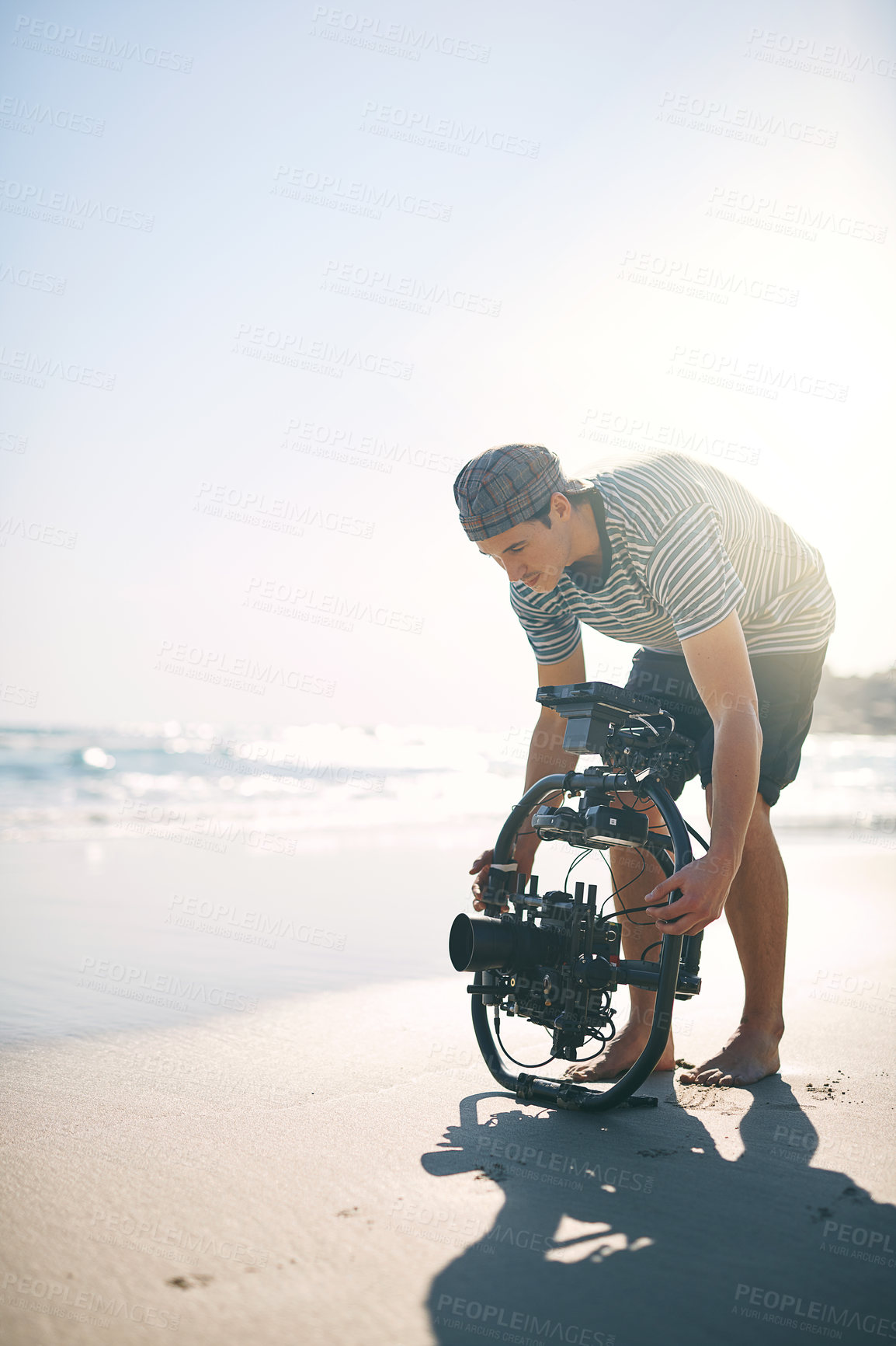 Buy stock photo Shot of a focused young man making a few adjustments on a state of the art video camera on a beach during the day