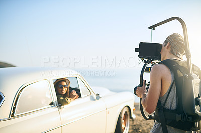 Buy stock photo Shot of a focused young man shooting a scene with people in a car with a state of the art video camera outside during the day