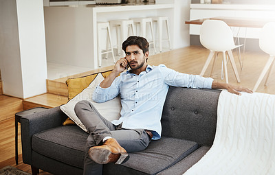Buy stock photo Cropped shot of a handsome young man making a phonecall while sitting on his sofa in the living room at home