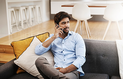 Buy stock photo Cropped shot of a handsome young man making a phonecall while sitting on his sofa in the living room at home