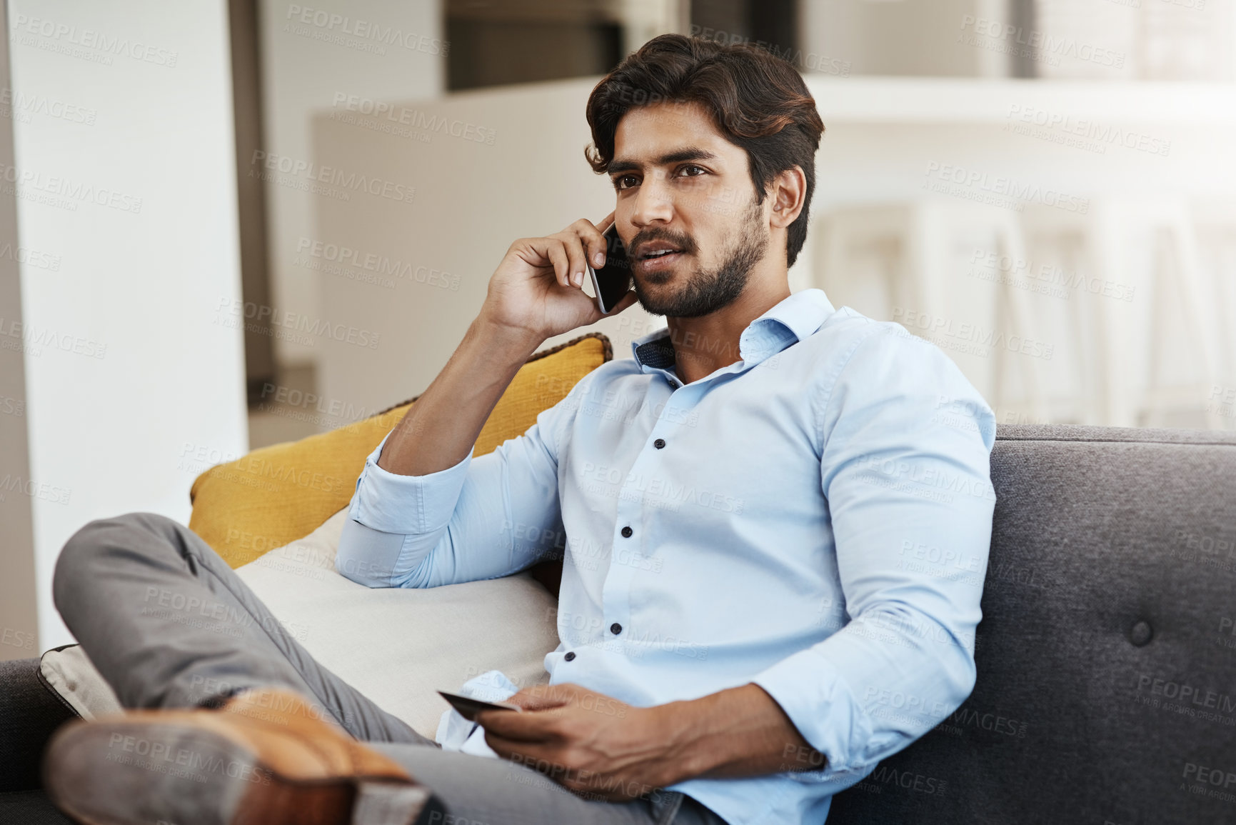 Buy stock photo Cropped shot of a handsome young man making a phonecall while shopping online on his sofa in the living room at home