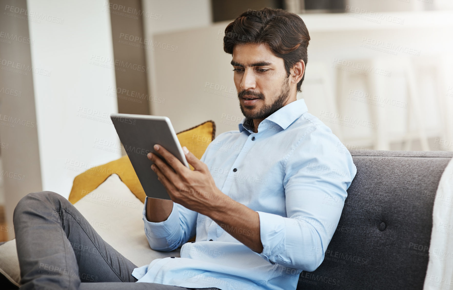 Buy stock photo Cropped shot of a handsome young man using his tablet while sitting on his sofa in the living room at home