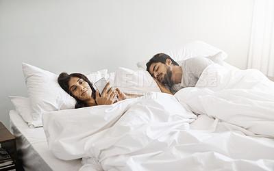 Buy stock photo Cropped shot of an attractive young woman sending text message while lying in bed beside her sleeping husband