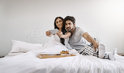 Buy stock photo Full length shot of an affectionate young couple taking selfies while having breakfast in bed