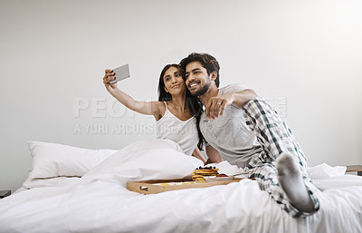 Buy stock photo Full length shot of an affectionate young couple taking selfies while having breakfast in bed
