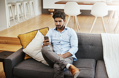 Buy stock photo Cropped shot of a handsome young man sending a text while sitting on his sofa in the living room at home