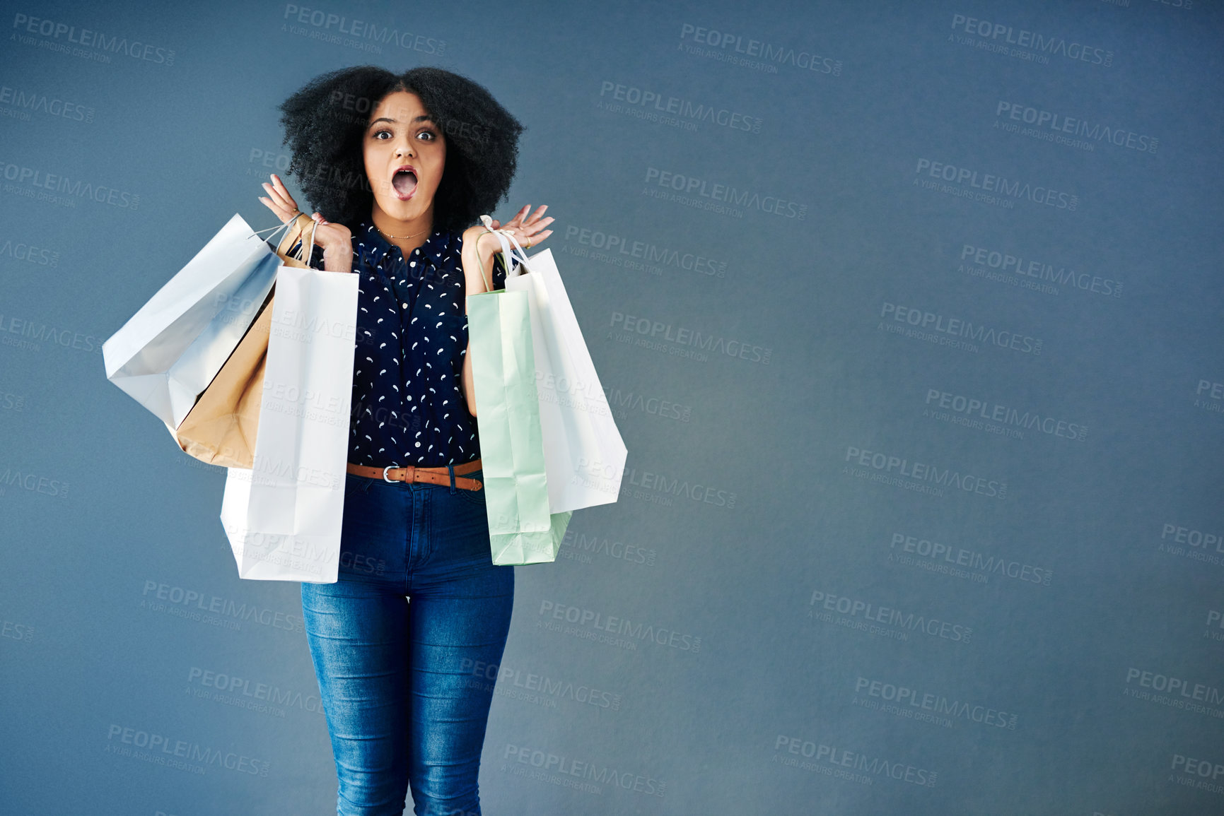 Buy stock photo Studio portrait of a young woman carrying shopping bags and looking surprised against a blue background