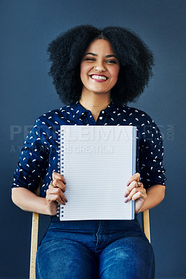 Buy stock photo Studio shot of a young woman holding up a blank notebook against a blue background