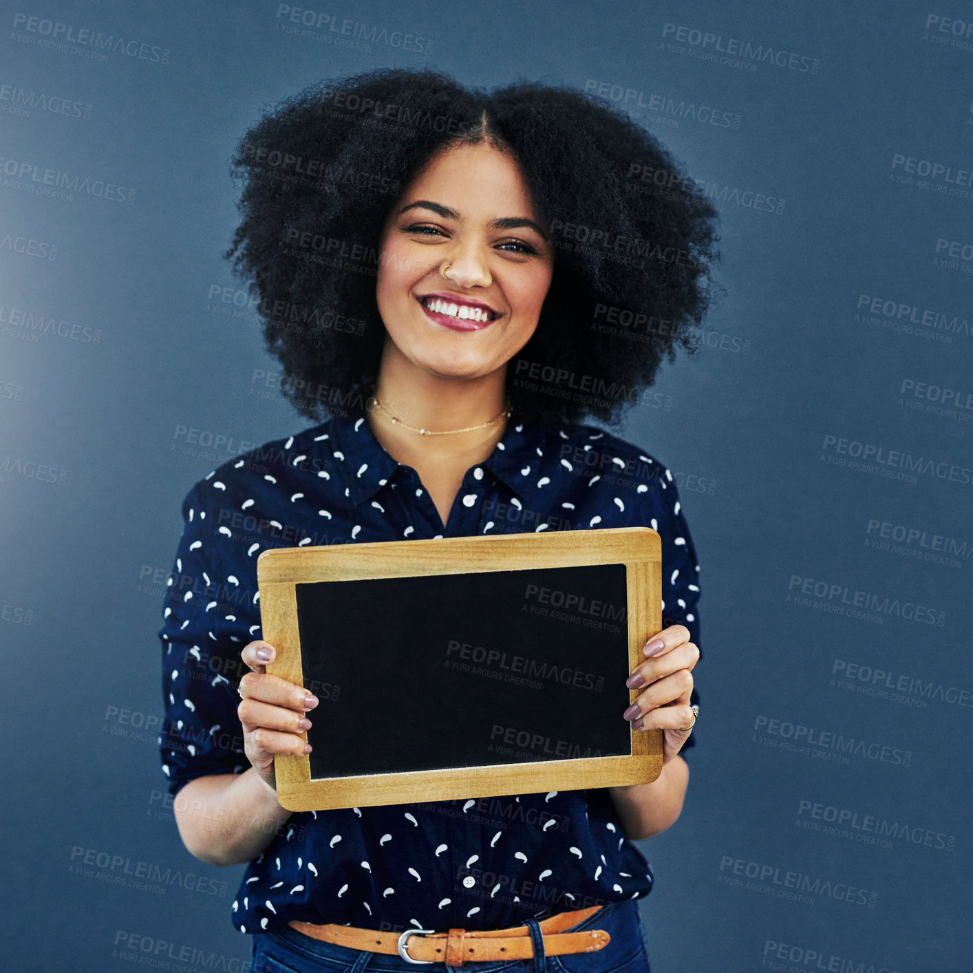 Buy stock photo Studio shot of a young woman holding a blank chalkboard against a blue background