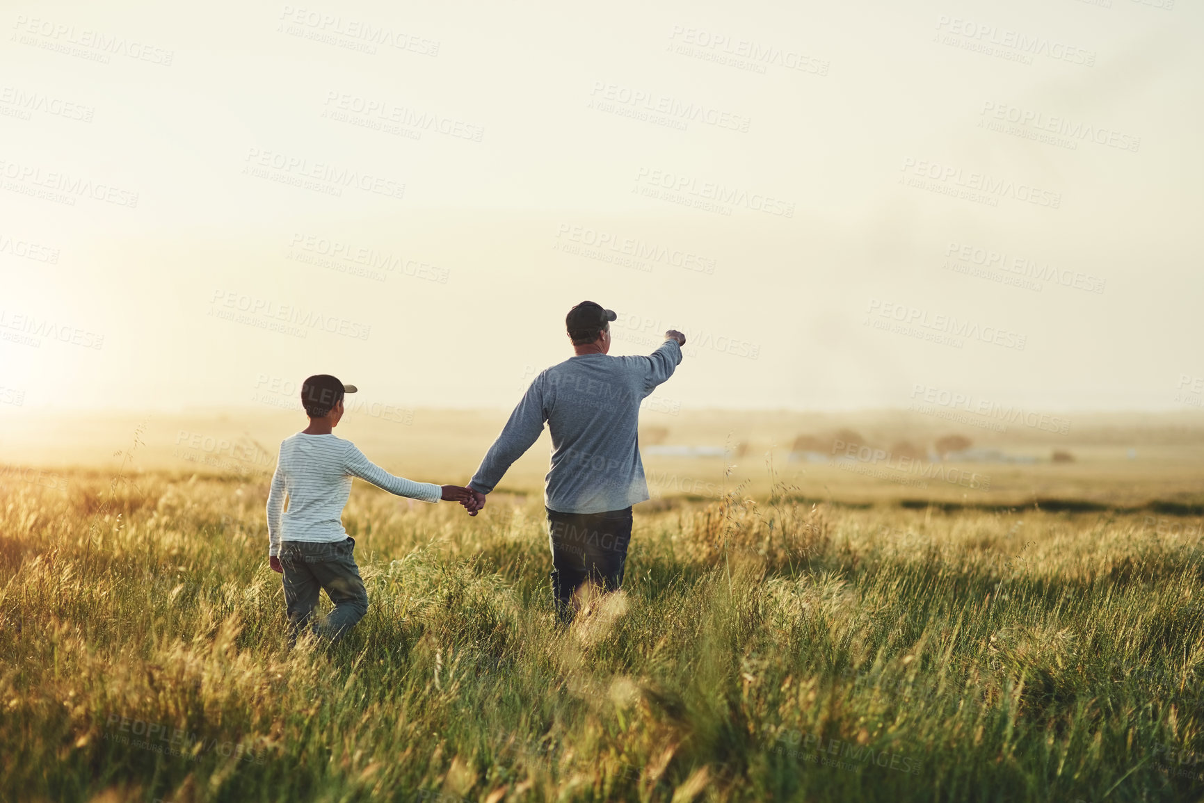 Buy stock photo Rearview shot of a father and his son walking on a field