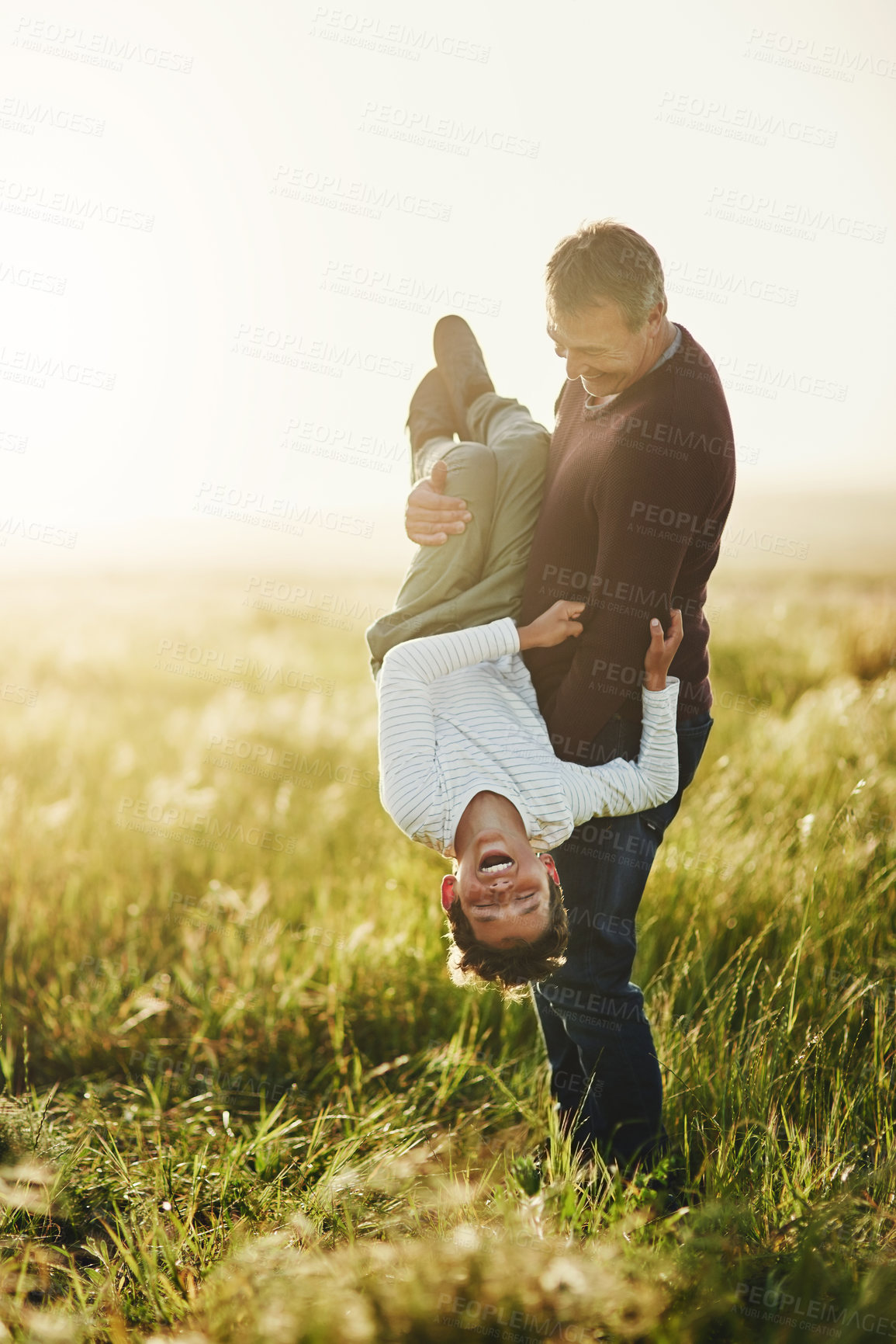 Buy stock photo Playful, man and carrying kid at grass field with laugh for outdoor adventure, silly and bonding together. Smile, father and son with humor in nature for funny, joke and love on holiday in Australia