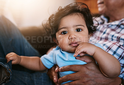 Buy stock photo Portrait of a cheerful little baby boy sitting on his dad's lap while looking into the camera at home during the day