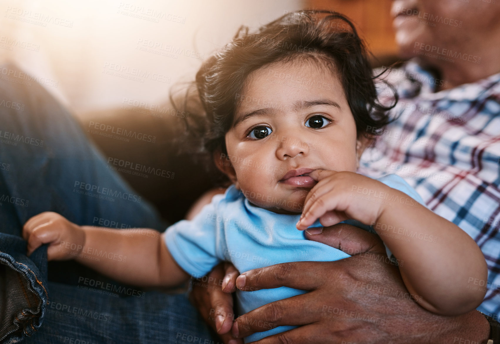 Buy stock photo Portrait of a cheerful little baby boy sitting on his dad's lap while looking into the camera at home during the day