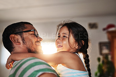 Buy stock photo Shot of a cheerful little girl being held in her father's arms inside at home during the day